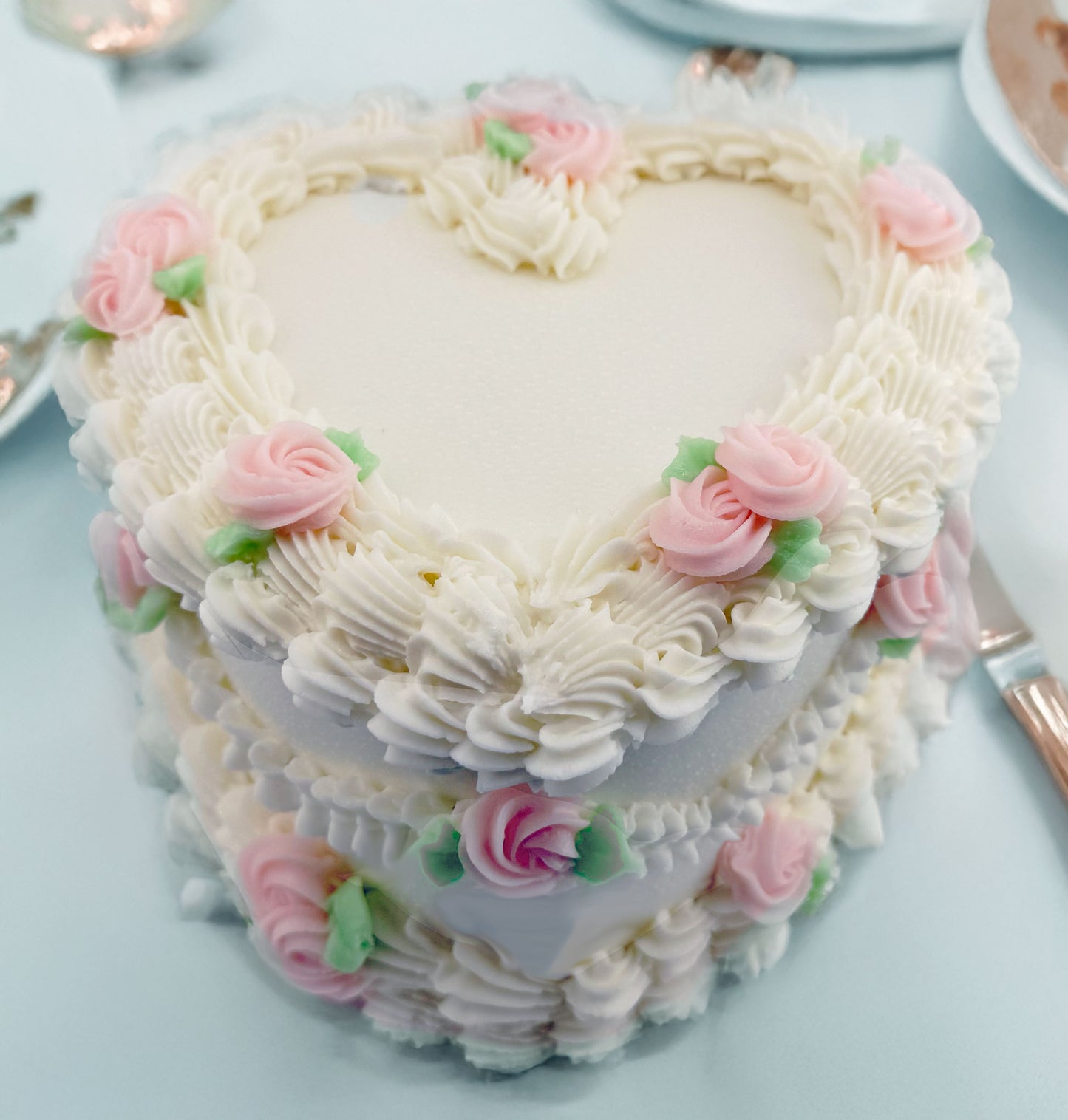 Heart-shaped cake with white frosting and pink flowers on a light blue background