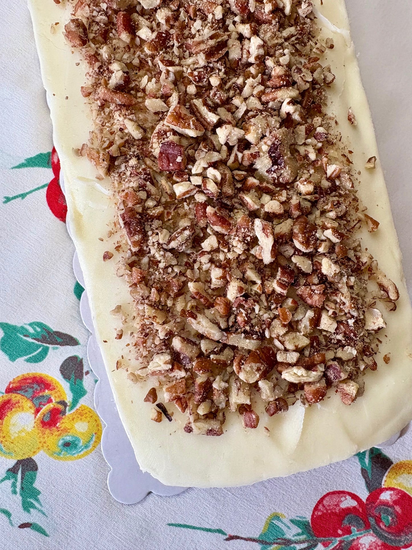 Unbaked bread loaf with pecans on top on a decorative tablecloth.