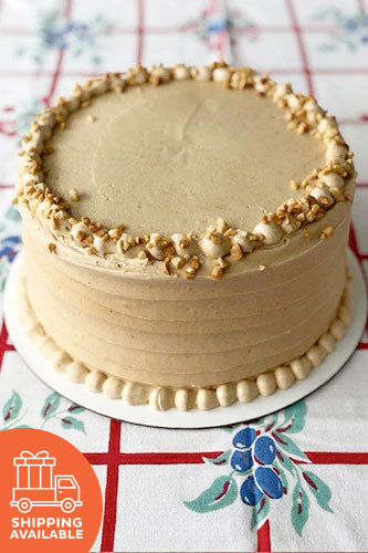 A chocolate peanut butter cake with peanut butter frosting and garnished with peanut crumbles, placed on a plate with a patterned tablecloth underneath.