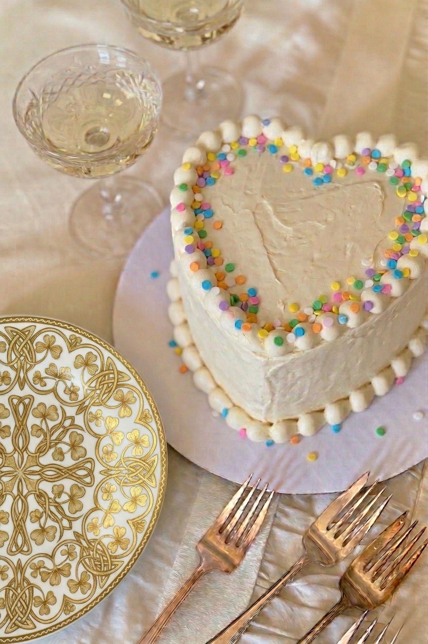 Heart-shaped cake with colorful sprinkles on a table setting with plates and glasses.