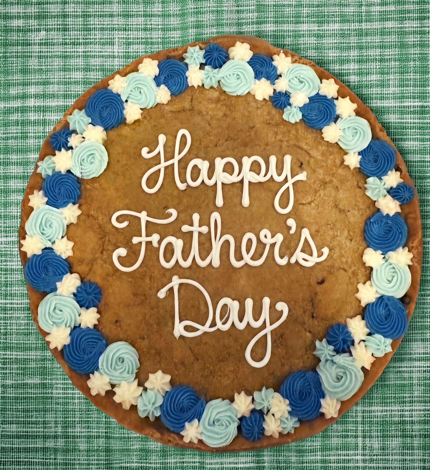 Cookie cake with 'Happy Father's Day' text and blue and white frosting on a green checkered background