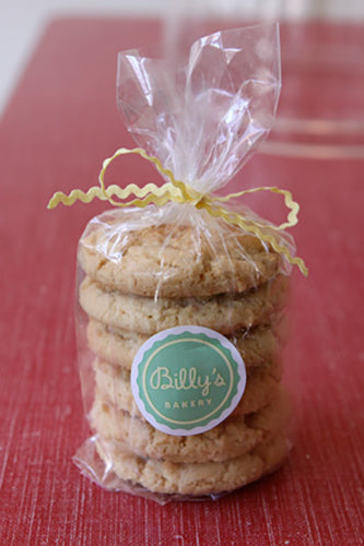 Stack of cookies in clear plastic wrap with a yellow ribbon on a red surface, featuring a 'Billy's Bakery' label.