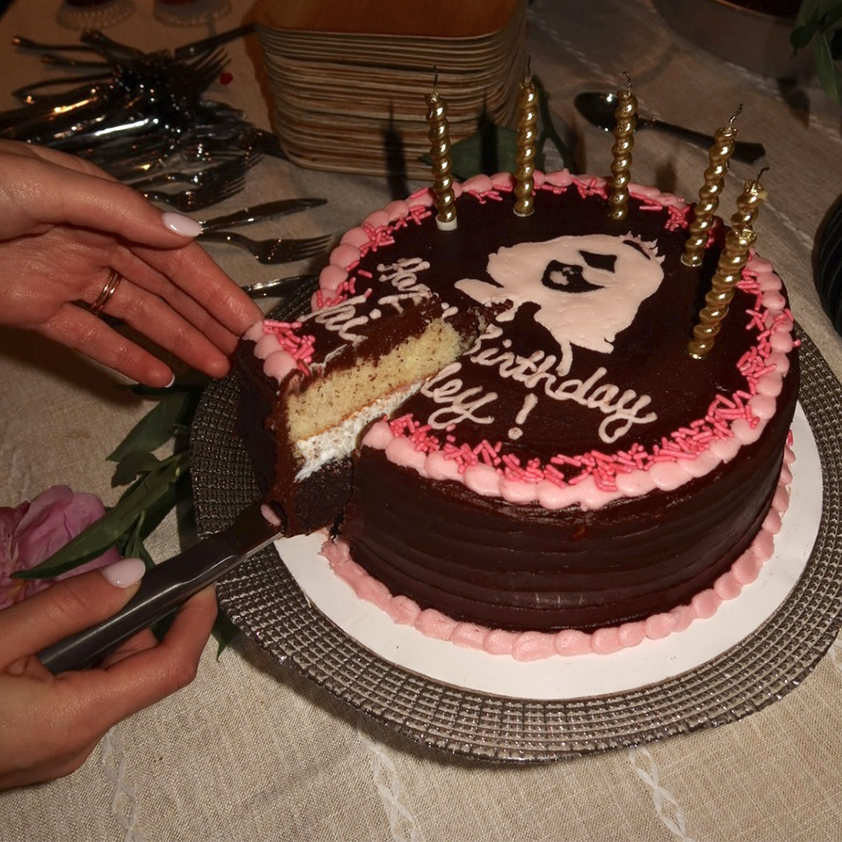 Chocolate birthday cake with pink frosting and lit candles being cut on a table.