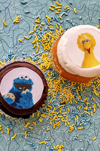 Two cupcakes with edible image frostings; one with a character from a popular children's show, the other with a solid color.