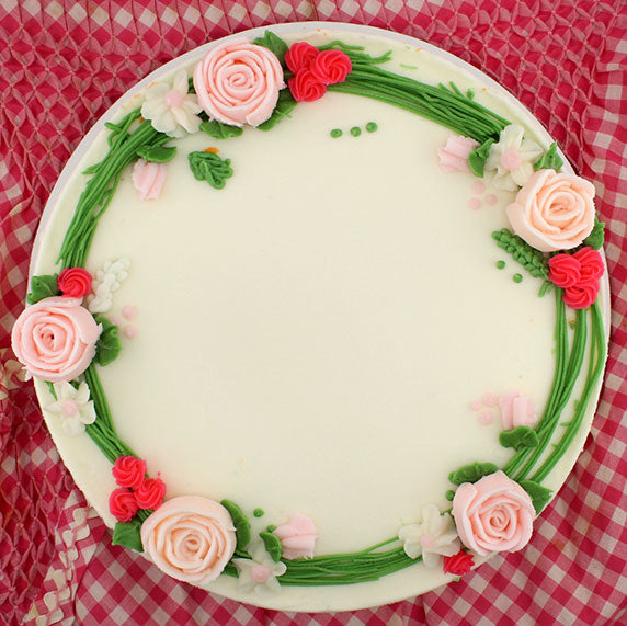 A round cake decorated with a garland of buttercream flowers in pink, red, and white colors, set against a red and white checkered background.