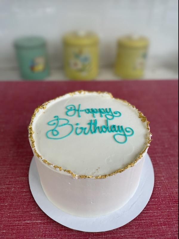 A round cake with a gold rim and the words 'Happy Birthday' written on top in a decorative font.