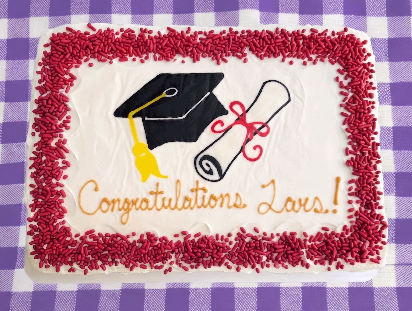 Graduation-themed cake with a cap, diploma, and 'Congratulations' text on a purple checkered background.