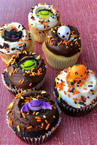 Halloween-themed cupcakes with decorative elements on a pink background
