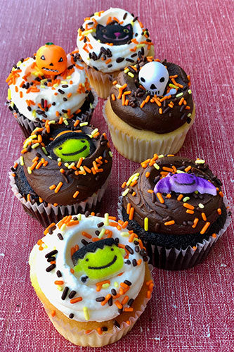 Halloween-themed cupcakes with decorative elements on a pink surface