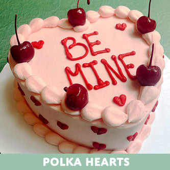 Pink cake with 'BE MINE' text and cherries on a green background