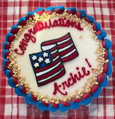 Decorative cake with 'Congratulations Archie!' text and American flag design on a red and white checkered background.