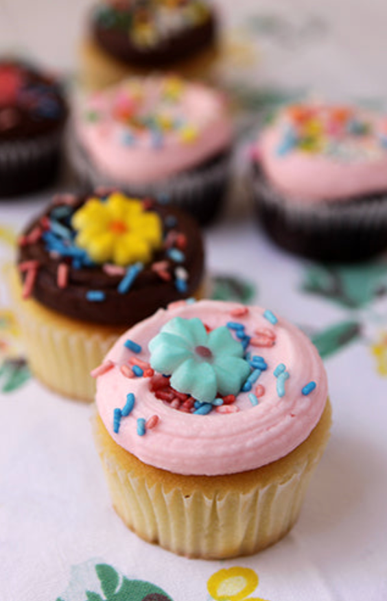 A variety of cupcakes with frosting and sprinkles, including both vanilla and chocolate flavors, garnished with different colored sugar decorations.