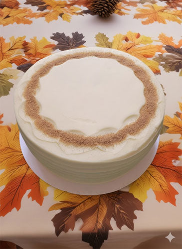 Pumpkin cake with cream cheese frosting and a ring of cinnamon sugar garnish on a table with autumn leaf tablecloth