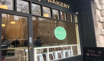Exterior view of Billy's Bakery Upper West Side, showcasing the storefront with large windows, the 'Billy's Bakery' sign, and a 'Now Open' sign on the sidewalk.