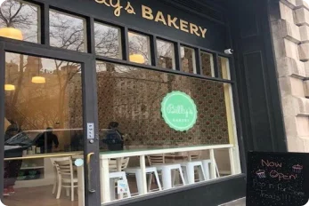 Exterior view of Billy's Bakery Upper West Side, showcasing the storefront with large windows, the 'Billy's Bakery' sign, and a 'Now Open' sign on the sidewalk.