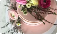 Pink tiered cake adorned with pink, yellow, and burgundy flowers and green foliage.