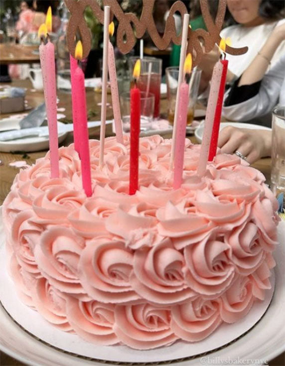 A pink rosette cake with multiple candles on top, served on a plate, indicating it is intended for a celebration such as a birthday or anniversary.