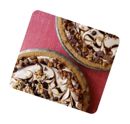 Two slices of Billy's Bakery Peanut Butter Chocolate Pie with whipped topping, chocolate drizzle, and peanut butter cups on a red surface.