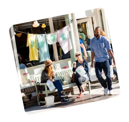 People enjoying coffee with shopping bags outside Billy's Bakery, with colorful t-shirts hanging on a line in front of the shop window.