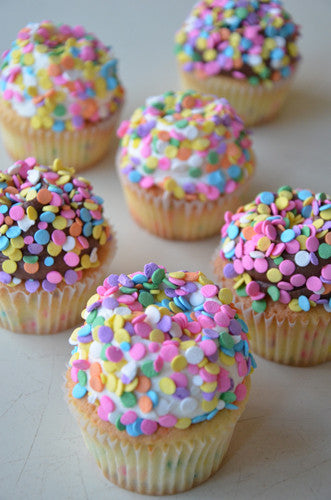 A group of cupcakes topped with multicolored sprinkles and confetti quins.