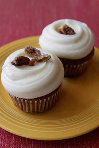 Two carrot cupcakes with cream cheese frosting and nuts on top, served on a yellow plate.