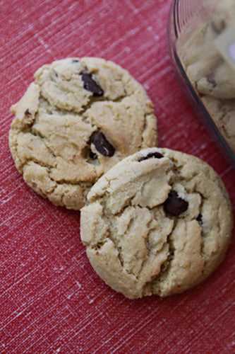 Two chocolate chip cookies on a red textured surface.