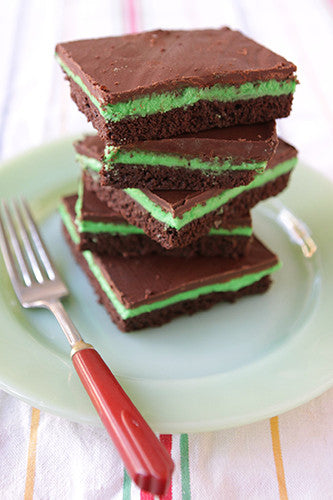 Stack of square mint chocolate brownies with a green mint layer and a dark chocolate top, next to a fork on a light green plate.