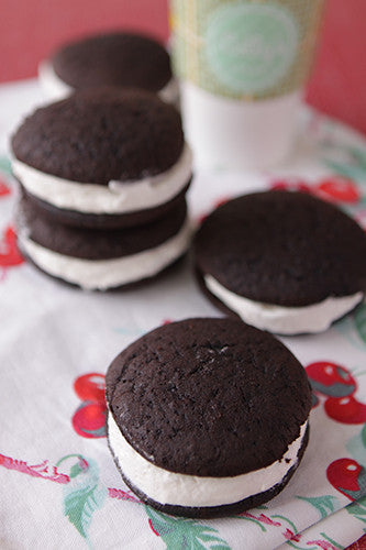 Stacked chocolate whoopie pies with marshmallow filling on a fabric with cherry design.