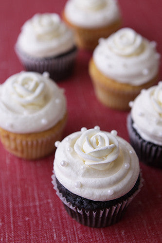 A collection of six cupcakes, some chocolate and some vanilla, topped with white frosting roses and white sugar pearl garnish.