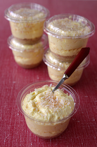 Vanilla pudding with coconut flakes topped with toasted coconut, served in a clear cup with a spoon on a red surface.
