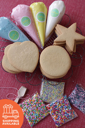 A variety of hand-cut sugar cookies decorated with royal icing, along with piping bags of icing and a mini spatula, displayed on a red surface.