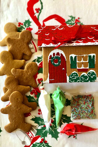 A variety of hand-cut sugar cookies in different shapes, with piping bags of royal icing and a mini spatula, displayed on a red surface with an instructional card.
