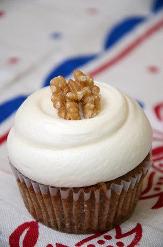 A gluten free carrot cupcake with cream cheese frosting and chopped pecans on top, placed on a cloth with red and blue patterns.