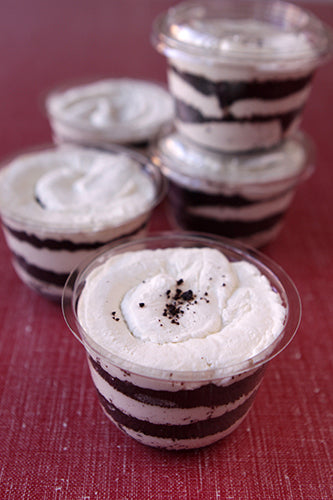 A stack of clear plastic cups filled with layers of whipped cream and chocolate wafer cookies, garnished with a dusting of powdered sugar.