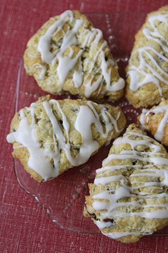 Five lemon cranberry scones with a white drizzle on top, placed on a red surface.