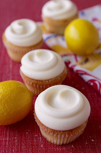 Lemon cupcakes with cream cheese frosting on a red surface, with lemons in the background.