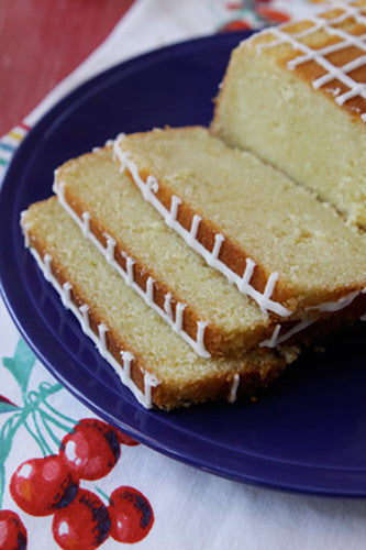A lemon loaf cake with a glazed top, served on a blue plate with a patterned napkin.