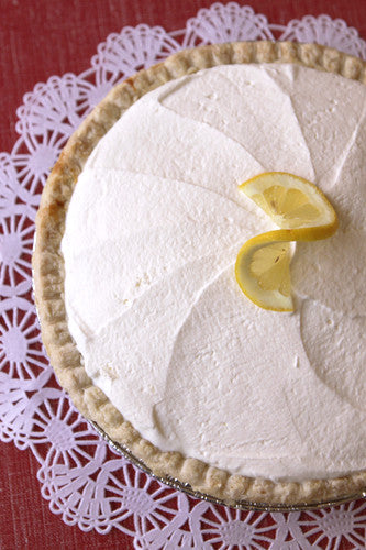 Lemon cream pie with whipped topping and lemon slices on a white doily.