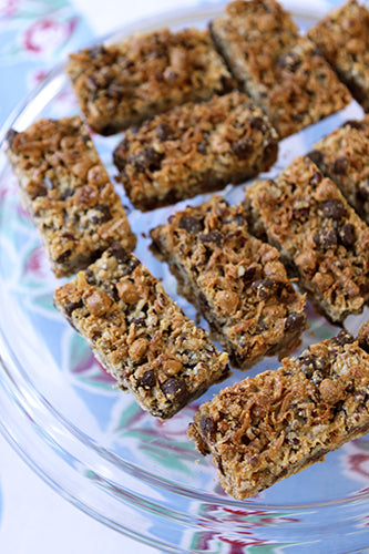Close-up shot of homemade granola bars with chocolate chips and nuts on a clear serving platter, arranged neatly.