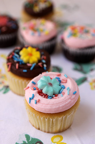 A variety of cupcakes with frosting and sprinkles, including both vanilla and chocolate flavors, garnished with different colored sugar decorations.