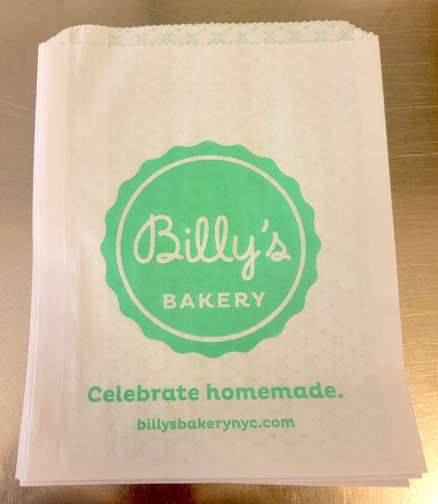 White paper bag with green Billy's Bakery logo and "Celebrate homemade. billysbakerynyc.com" text