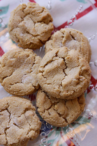 A photo of peanut butter cookies on a surface with a red and green pattern. The cookies appear to be golden brown in color and have a dusting of sugar on top.