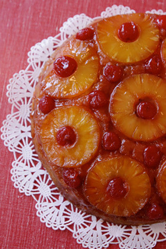 A pineapple upside down cake with brown sugar and cherries baked in a cast-iron skillet, presented on a lace doily.
