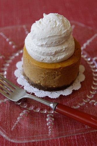 A piece of pumpkin cheesecake with whipped cream on top, served on a plate with a red fork and a white napkin.