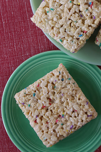 Square marshmallow rice krispie bars with rainbow sprinkles on a green plate.