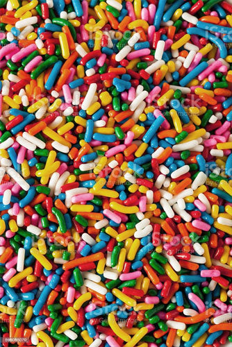 A variety of colorful sprinkles spread out, ranging in colors such as red, yellow, blue, green, purple, and white.