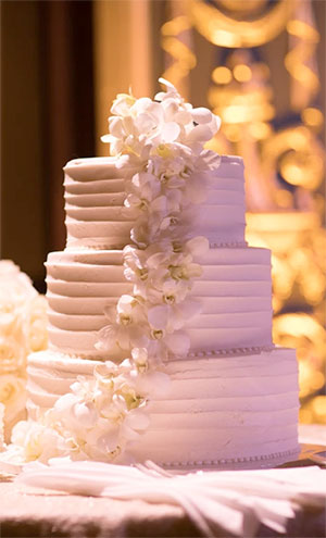Three-tiered white wedding cake adorned with a cascading arrangement of white orchids.
