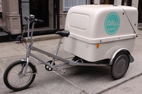 A white delivery bicycle with a covered container attached to the back, branded with 'Billy's Bakery'.