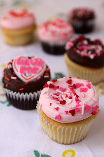 A selection of Valentine's Day cupcakes with various toppings and frosting, including sprinkles and heart-shaped sugar decorations.