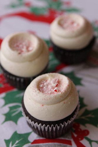 Three chocolate cupcakes with white frosting and a candy cane crumble topping, placed on a holiday-themed napkin.
